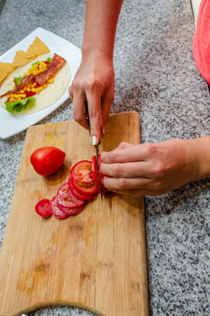 Woman's hands cutting a tomato on a counter to prepare a dish