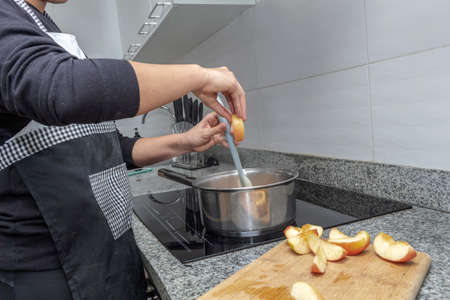 Hands cooking caramelized apples in a pot on an induction cooker. Process for preparing an apple cakeの写真素材