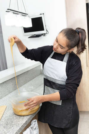 Girl to teenager mixing the dough for a cake. The dough falls from a spoon. Process for making apple...