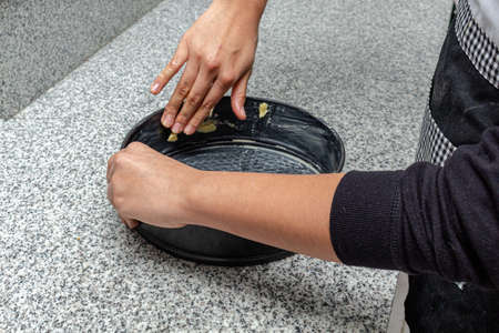 Hands greasing a cake pan on a kitchen counter in the house. Process for caramelized apple pie