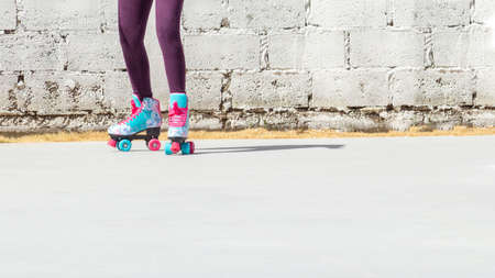 Legs of a girl with colorful roller skates on a white brick background