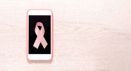Pink cell phone with breast cancer prevention tape on a light wood background. Top viewの写真素材