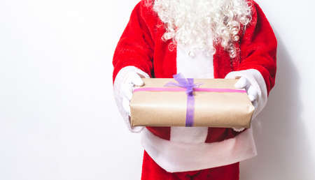 Santa Claus whose bearded face is unrecognizable offering a gift with his two hands at Christmas on...