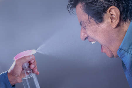 Hand with an alcohol gel dispenser throws a spray on a man's face to disinfect it. Biosafety concept