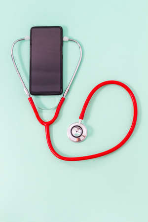 Top view of a red stethoscope with red stethoscope headset on green background. Medical and communications concept or cell phone repair.の写真素材