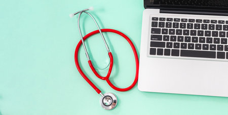 Red stethoscope rolled up next to a laptop on a background with good pastel green copyspace. Technology and medicine conceptの写真素材