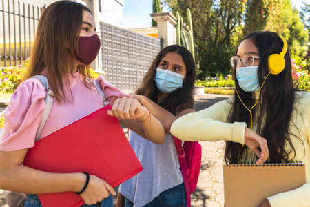 Close-up of three teenage Latina friends with masks, salute with the elbow in the back to school for the prevention of the virusの写真素材