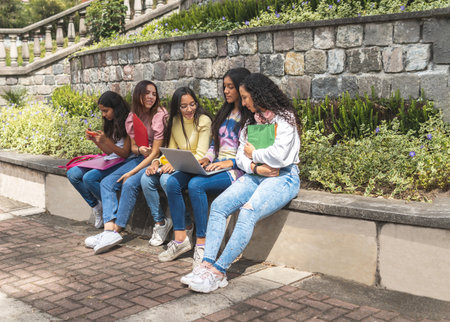 Group of Latina teen girls students walking along a path in a park or schoolyard at the back to school with notebooks and backpacks. Education and teens conceptの写真素材