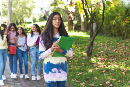 Selective focus of dark skinned teenage female student with her books in her arms looking at camera...