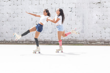 Two friends in shorts, white t-shirt and long socks skate fun on roller skates on a summer morningの写真素材