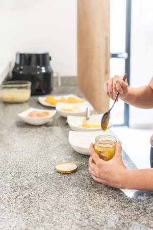 Close-up of hands taking honey from a container next to other ingredients on the kitchen counterの写真素材