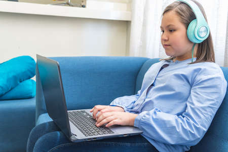 Blond girl with hearing aids using her laptop sitting on a blue sofa