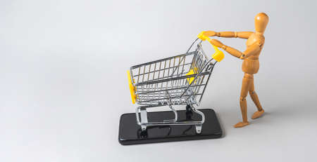 Wooden human figure with a miniature shopping cart on a cell phone. Online shopping conceptの写真素材