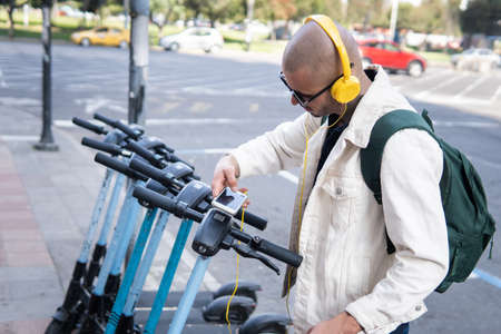 Bald Latin man taking a public scooter with an app on his cell phone
