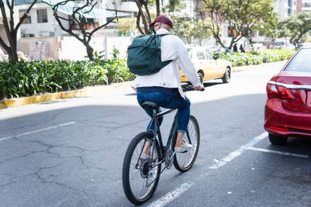 Young man with a backpack on his back riding a bicycle on a city streetの写真素材