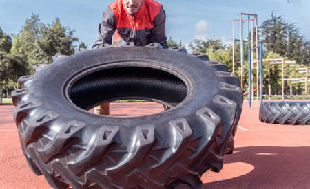 Young man lifting and pushing a huge tire working out with functional exercise outdoors