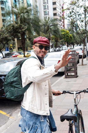 Man with glasses, backpack and red cap greets walking with his bicycle on a city street