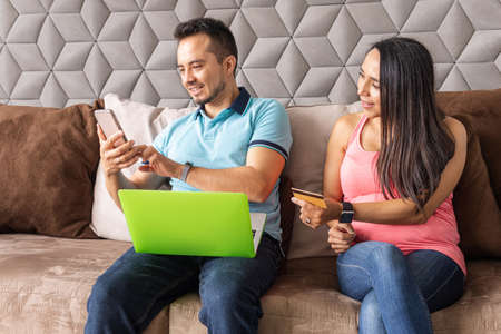 Latin couple at home shopping online with their credit card on their laptop and smart phone