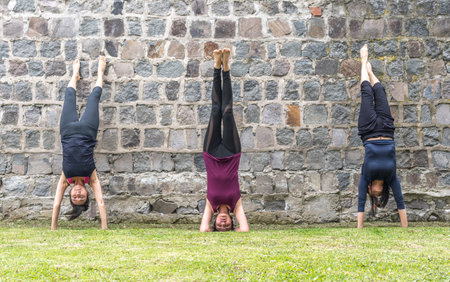 Three women standing handstands on a wall practicing yoga in the morning outdoors