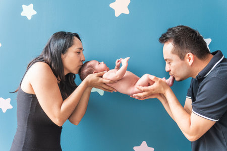 Latino mother and father hold their baby in their hands giving him a kissの写真素材