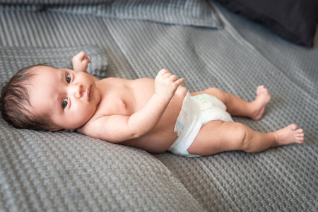 baby looking at camera lying on a diapered bedの写真素材