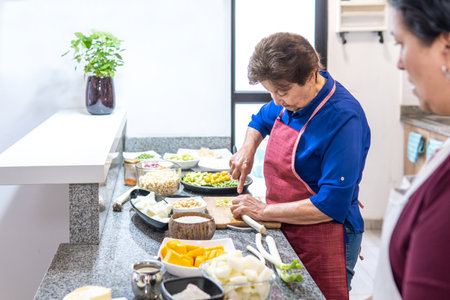 An elderly woman cooks while her adult daughter accompanies herの写真素材