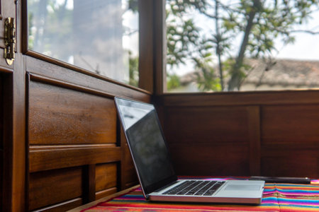 Laptop and cell phone on a colorful desk next to a window and wooden wallsの写真素材