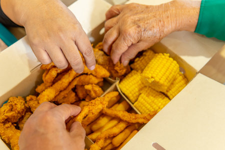 closeup of three hands taking food from a fast food box with chicken, corn, french fries and arepasの写真素材