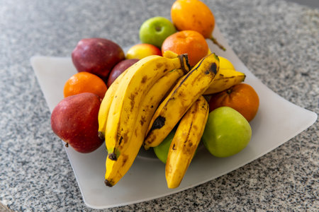 fruit bowl with bananas, green apples, red apples and tangerines on a granite surfaceの写真素材