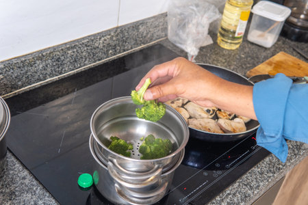 man's hand placing broccoli in a steamer on an induction cookerの写真素材