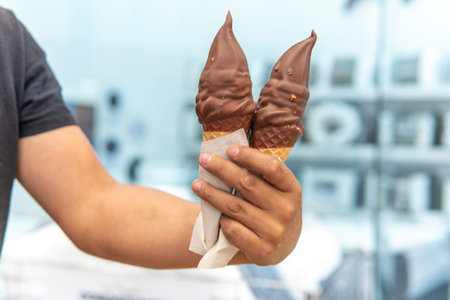 Man's hand holding two chocolate covered cream ice creams in cone