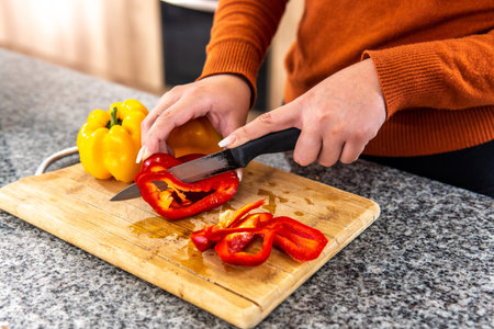 close-up of woman's hands cutting peppers on a cutting board at the kitchen counterの写真素材