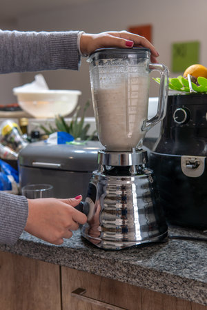 Close-up of a woman activating a blender to prepare a smoothie on a kitchen counterの写真素材
