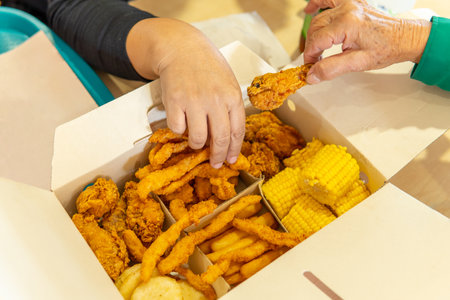 hands of two women take food from a fast food box with chicken, corn, french fries and arepas in a food courtの写真素材
