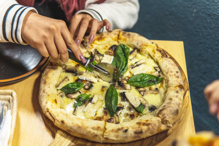 close-up of a woman's hand cutting an artisanal pizza with basil on a tableの写真素材