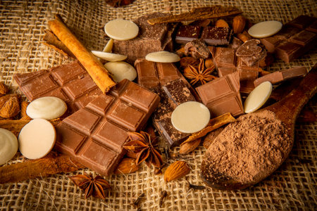Variety of chocolate, light and dark with white chocolate and spices with almonds on a textured backgroundの写真素材