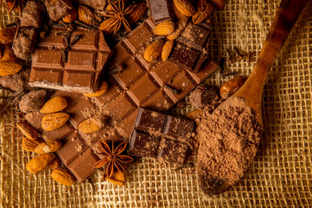 Overhead shot of chocolate pieces of different varieties with almonds and spices on a rustic backgroundの写真素材
