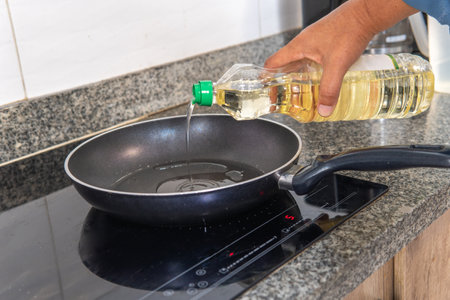 hand putting oil in a frying pan on an induction cooker in the kitchenの写真素材