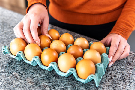 woman's hands taking an egg from a bucket on the kitchen counterの写真素材