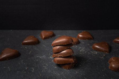 Heart shaped chocolate stacks on black background. Still life, love and chocolate concept