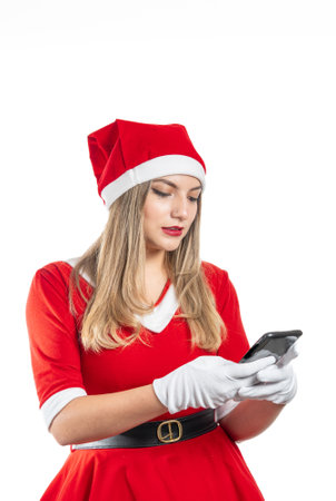 Young woman dressed as Santa Claus sending a text message on a smart phone. Vertical photography of christmas and technology on white backgroundの写真素材