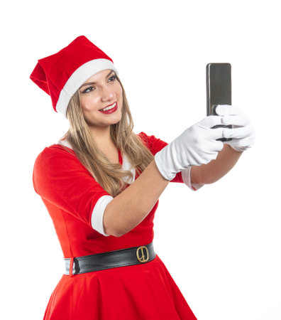Young woman dressed as Santa Claus smiling looking at a cell phone on white backgroundの写真素材