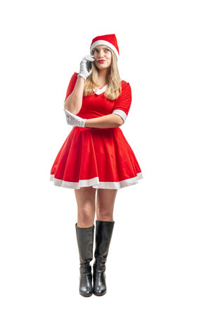 Mother Christmas standing talking on the cell phone. Mama Claus thoughtful in a conversation on smart phoneの写真素材