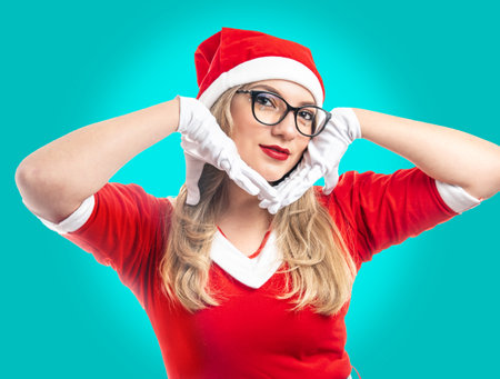 Young blonde haired woman dressed as Santa Claus with glasses looking at camera isolated on turquoise backgroundの写真素材