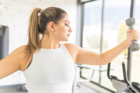 Young latin woman looking at her arm while lifting a dumbbell during exercise in a gymの写真素材