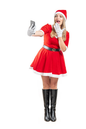 Young latin woman santa claus looking shocked watching something on her cell phone with hand on open mouth at christmasの写真素材