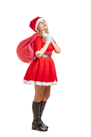 Young blonde woman Santa Claus walking thoughtfully with a bag of gifts at Christmas isolated on white backgroundの写真素材