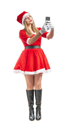 Young woman Santa Claus blowing a kiss to someone on cell phone isolated on white backgroundの写真素材
