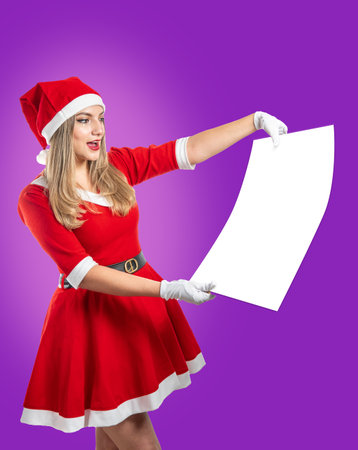 Young female Santa Claus looks in amazement at a poster with space for text on a purple backgroundの写真素材