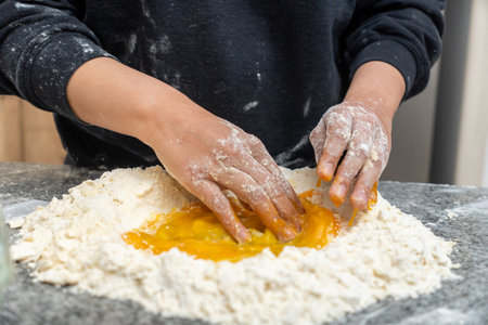 Close-up of young woman's hands mixing eggs and flour on a counter in the kitchenの写真素材